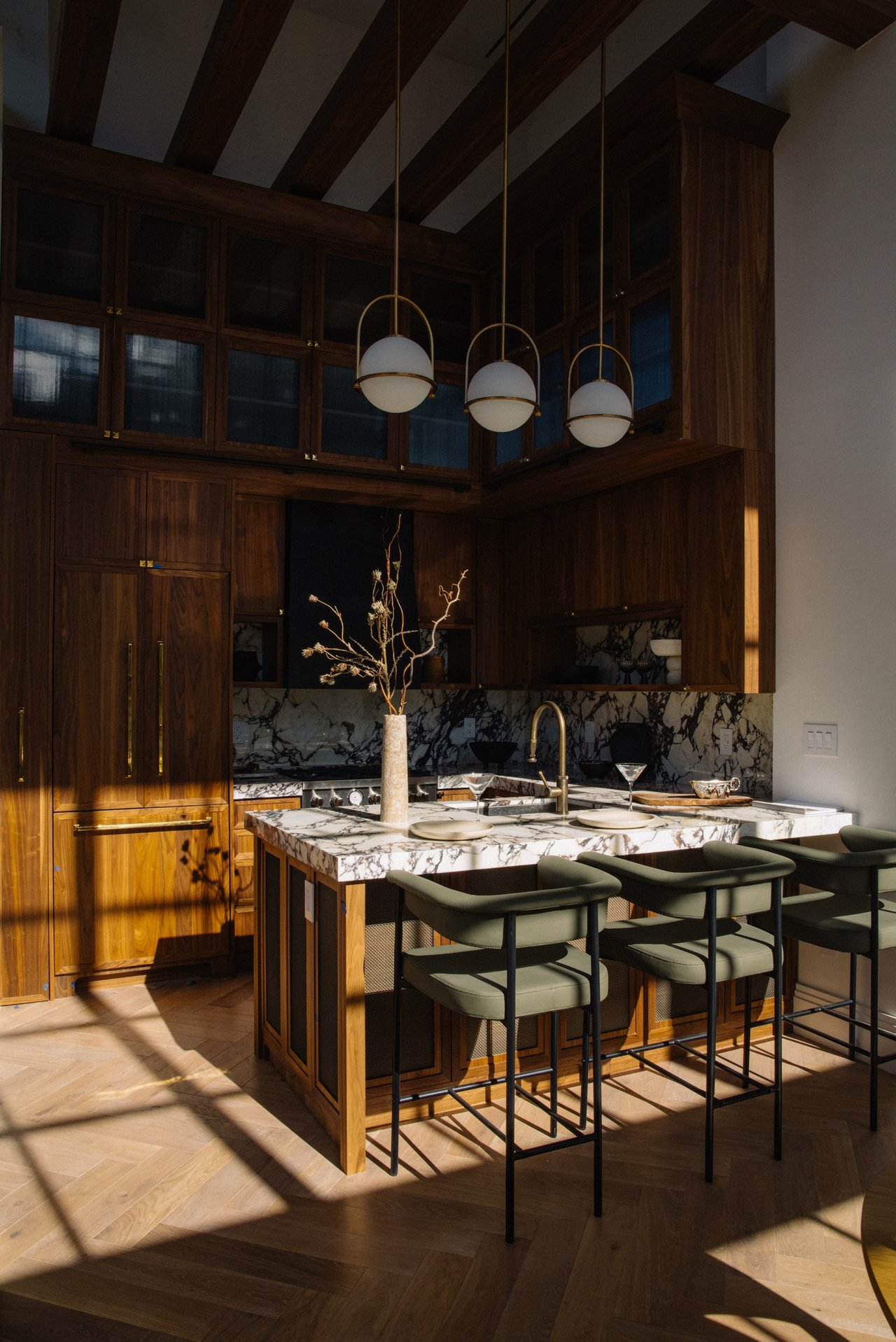 Kitchen with walnut cabinetry, a veined marble island, green bar stools, and globe pendant lights.