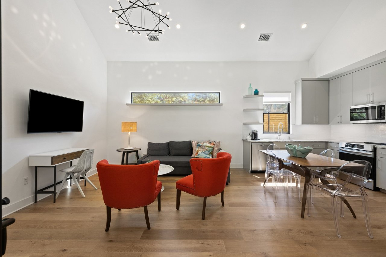 Open-plan living and dining area with red armchairs, a dark sofa, and a modern gray kitchen.