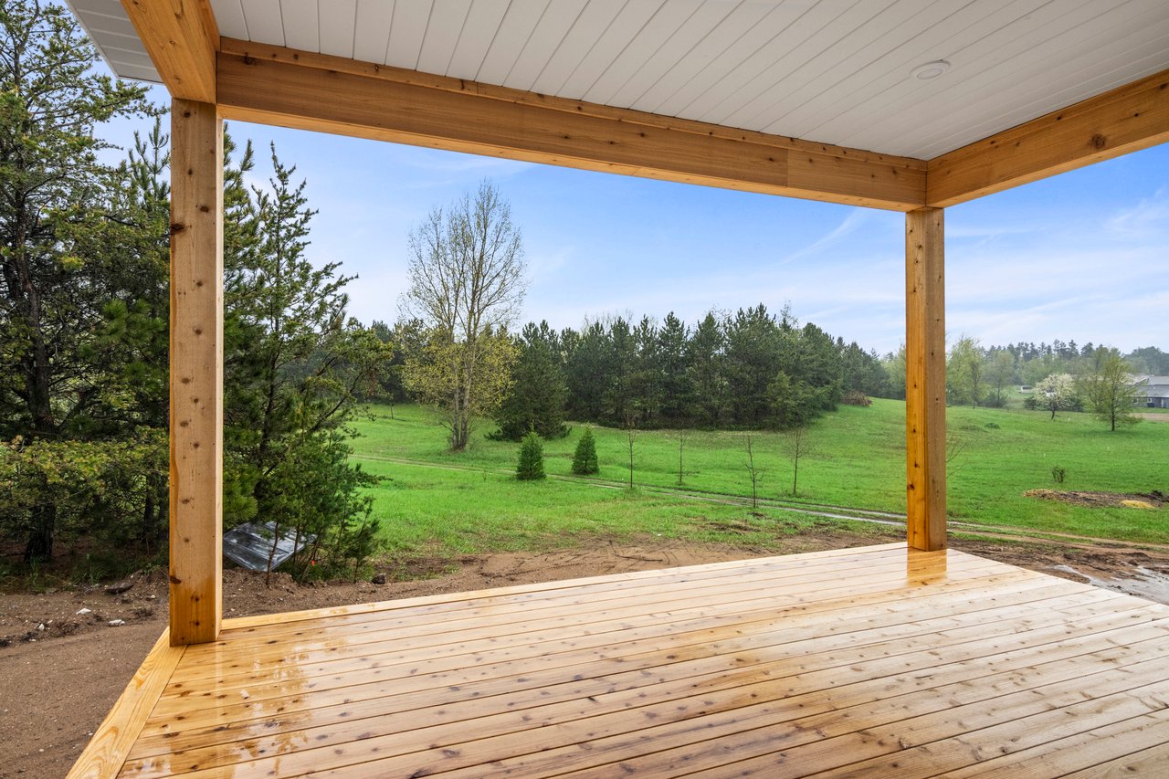 Covered wooden porch overlooking a green lawn and wooded edge.