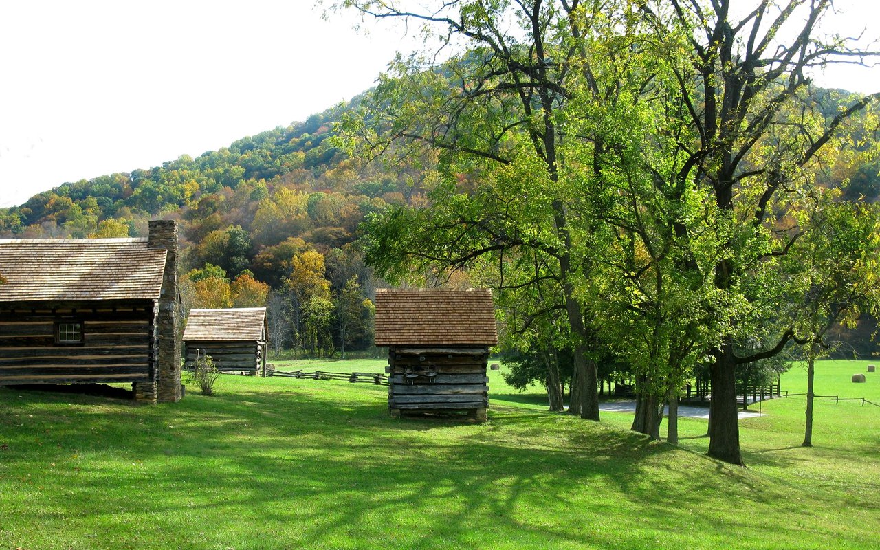 Weaverville landscape with historic log cabins, green fields, and a wooded autumn hillside.