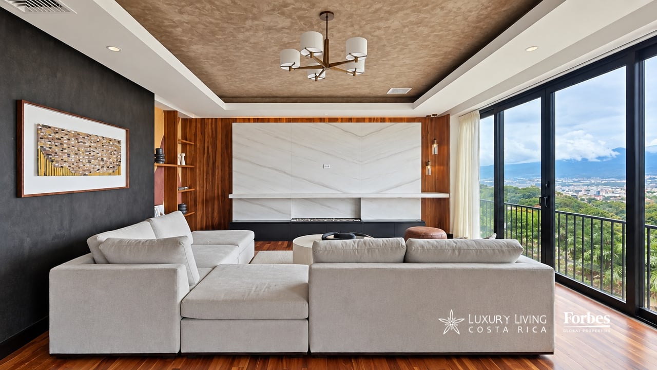 Penthouse living room with a white sectional, marble fireplace, and balcony overlooking the city and mountains.
