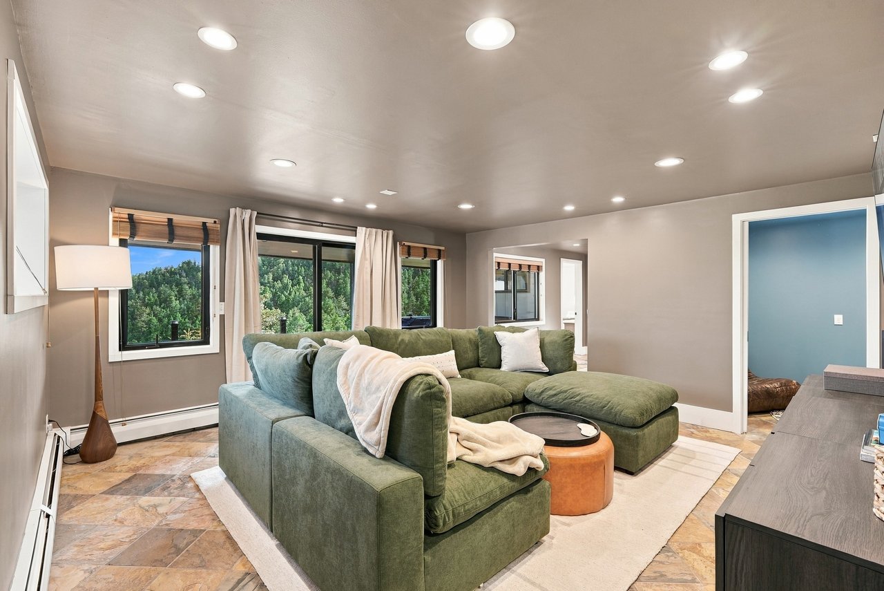 Living room with a green sectional sofa and windows overlooking trees.