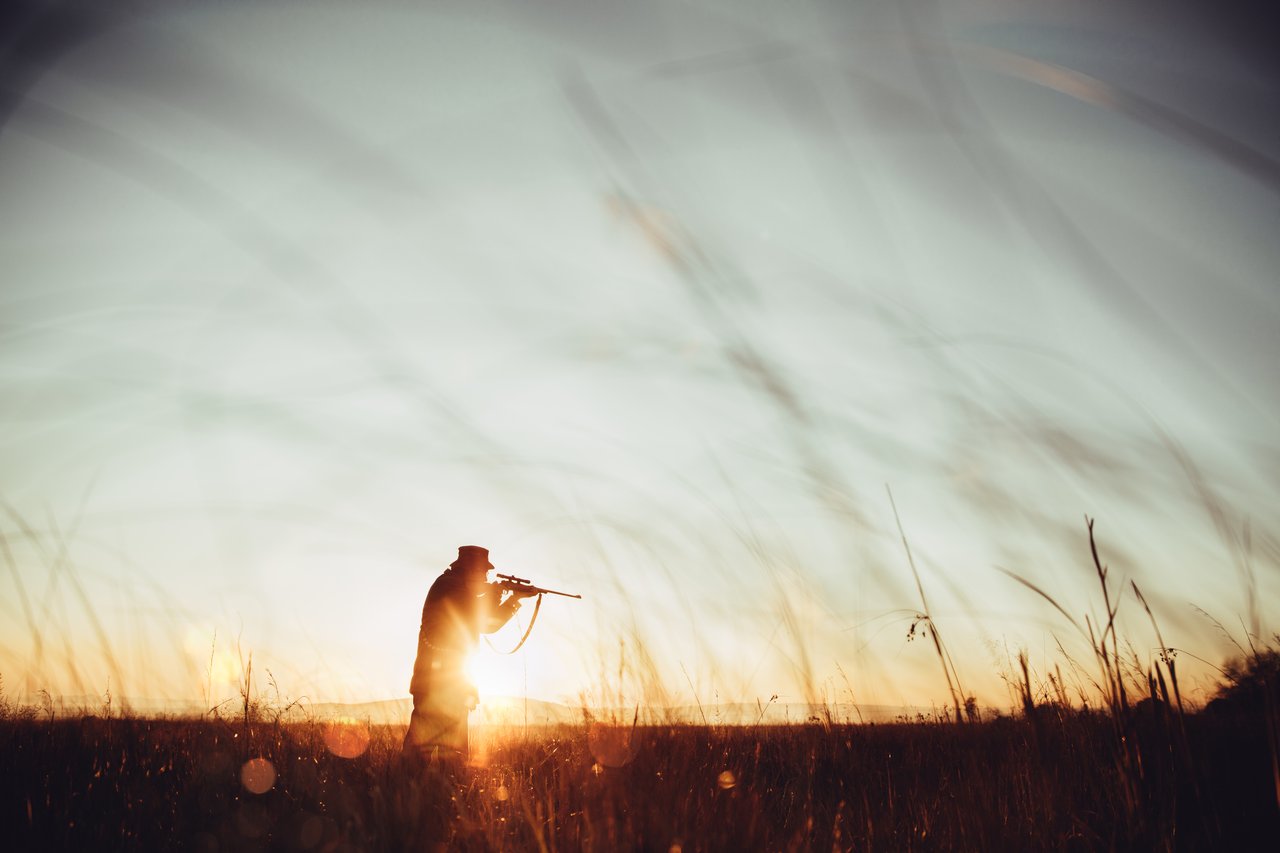 Silhouette of a hunter tracking wildlife in a field at sunrise, highlighting specialized outdoor sports gear and hobby storage.