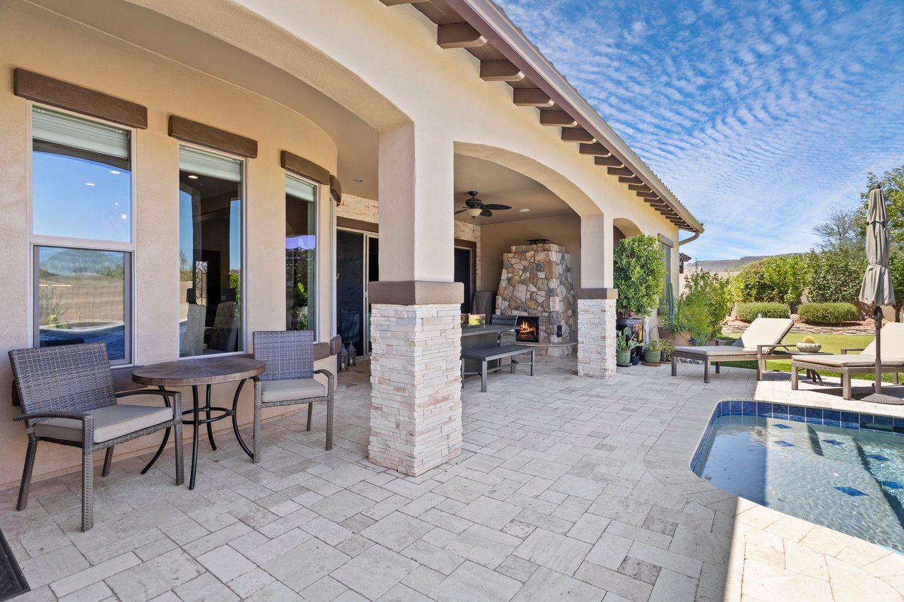 Covered backyard patio with stone fireplace, outdoor furniture, and a pool beside the home.