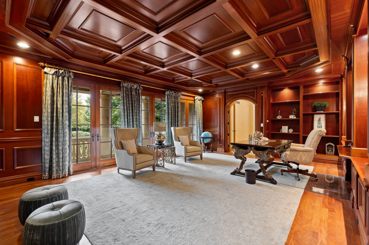 Mahogany-paneled home office with a coffered ceiling, built-in shelves, and French doors.