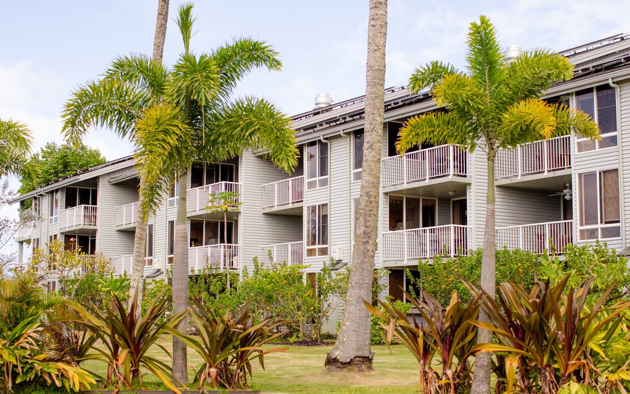 Haiku Plantation residential building with white-railed balconies framed by palms and tropical landscaping.