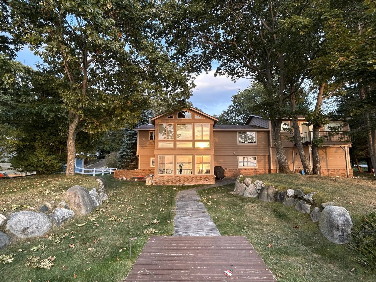 Lakefront home with a broad window wall, wooded yard, and boardwalk leading to the house.