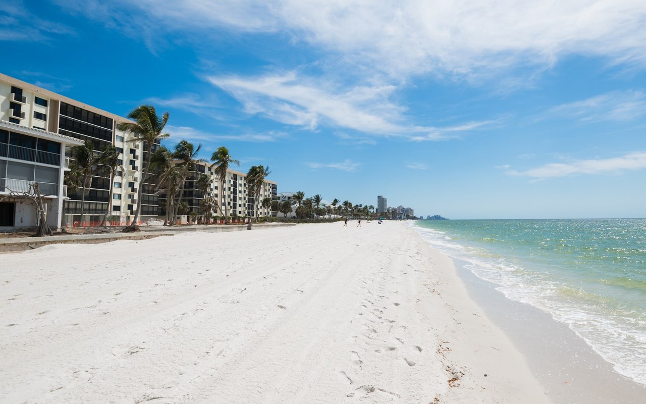 Beachfront condominiums beside a broad white-sand beach and turquoise water.