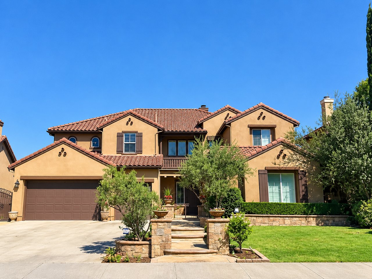 Two-story stucco home with terracotta tile roofs, a double garage, and landscaped stone entry steps.