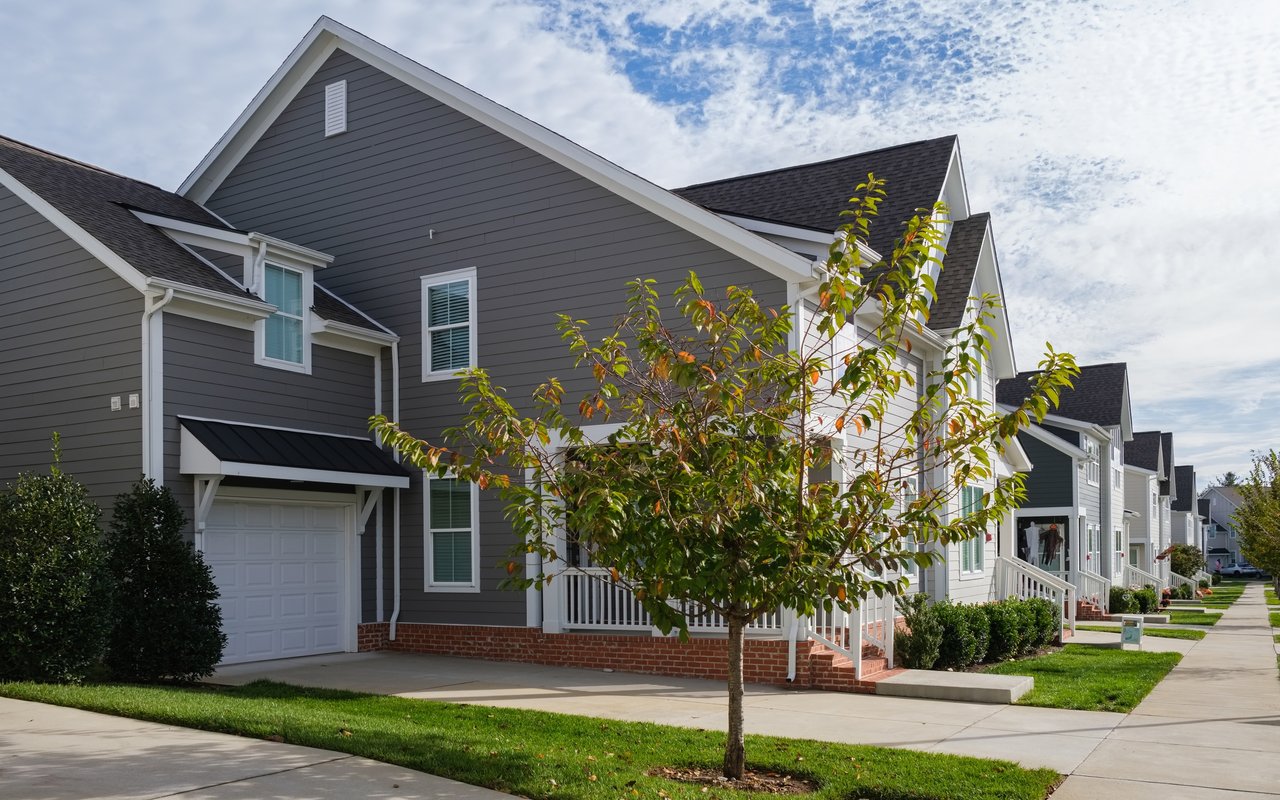 Attached two-story homes with contrasting siding, front porches, and a young tree with orange leaves.