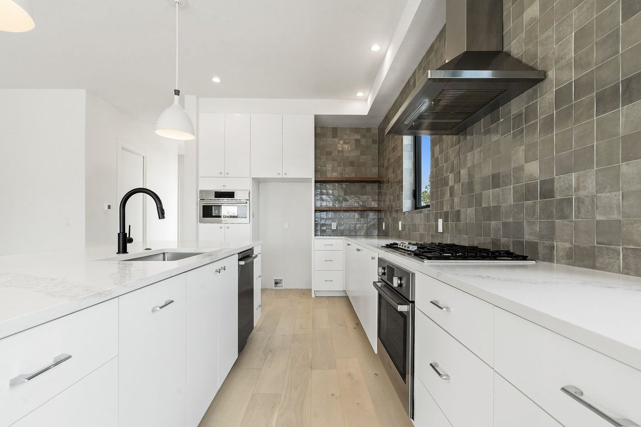 Modern kitchen with white cabinets, gray tile backsplash, and pale wood floors