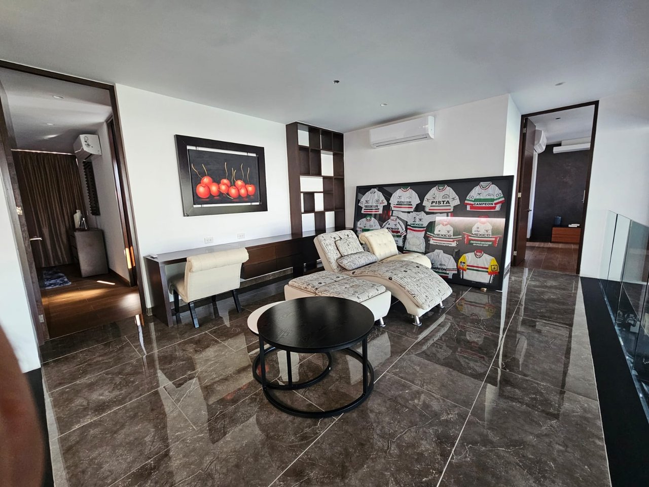 Living room with cream lounge chairs, glossy dark tile floors, and a display of Mexico cycling jerseys.