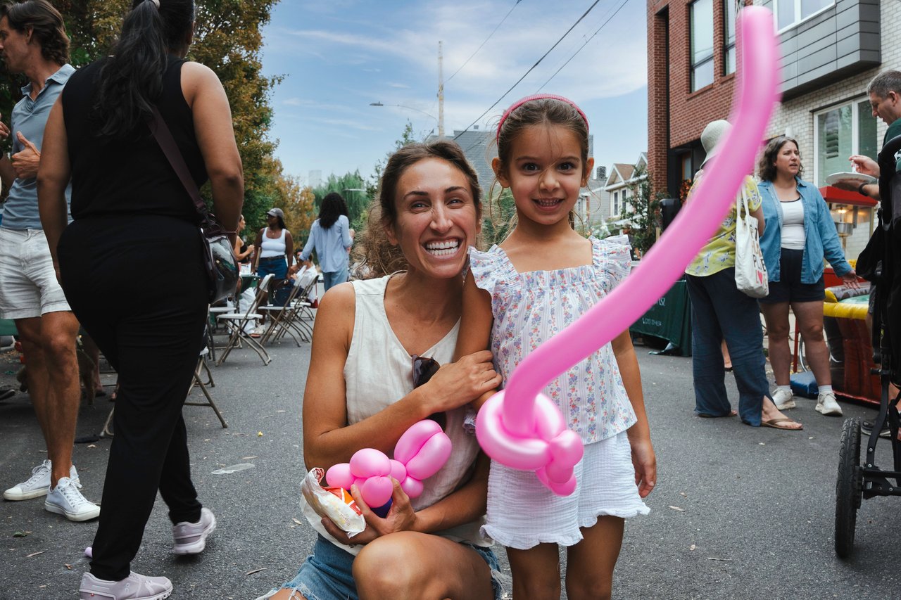 Woman and young girl at a neighborhood block party, holding pink balloon art.