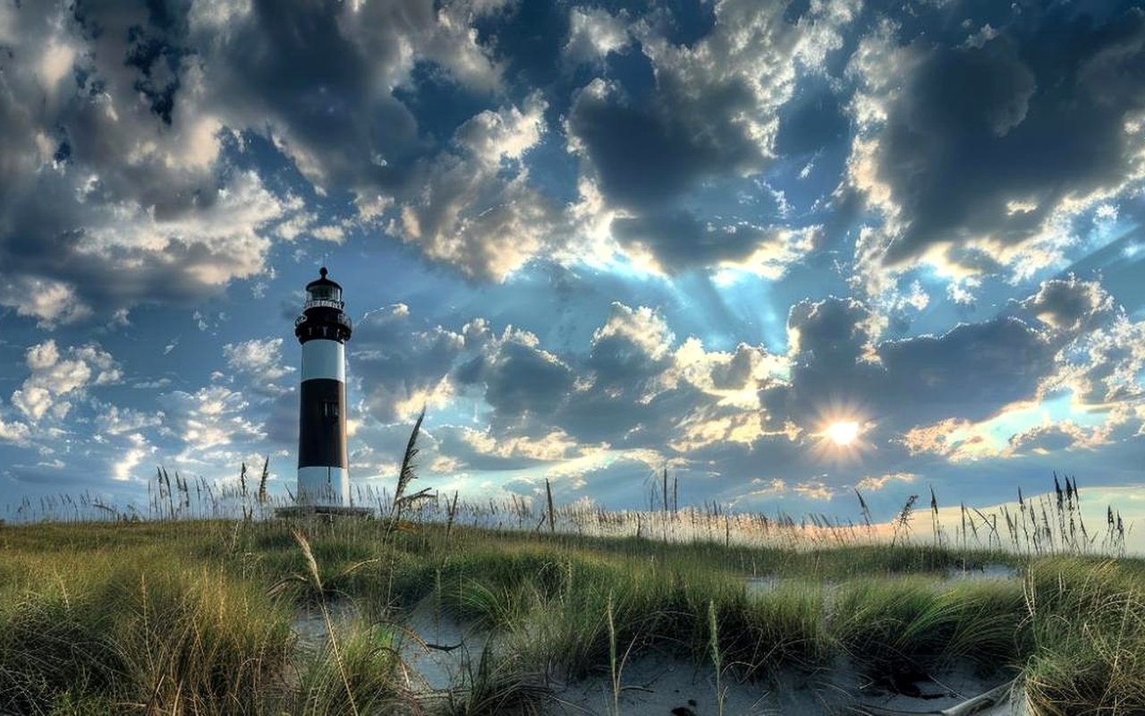Fire Island Lighthouse rises above grassy dunes beneath a dramatic sunset sky.