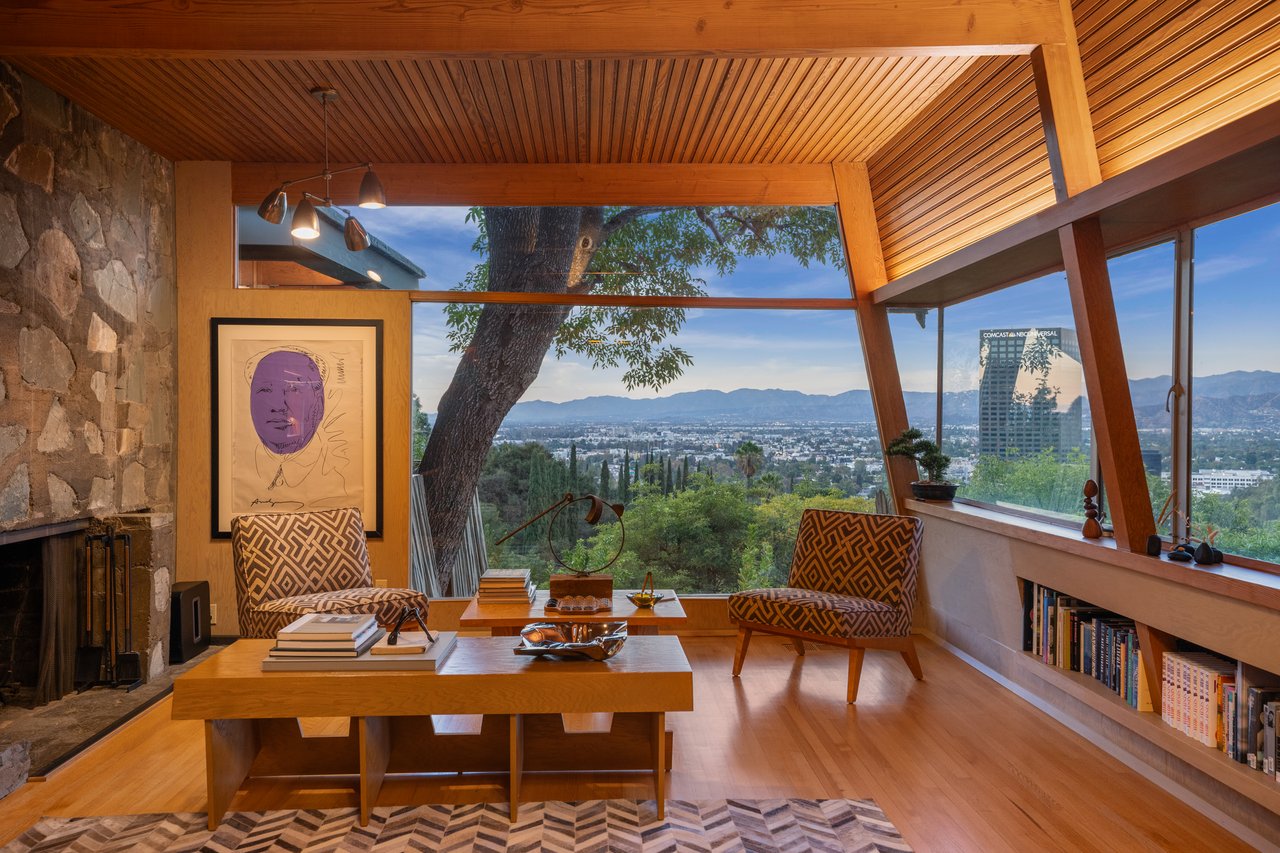 Living room with a stone fireplace and broad city and mountain views through large windows.