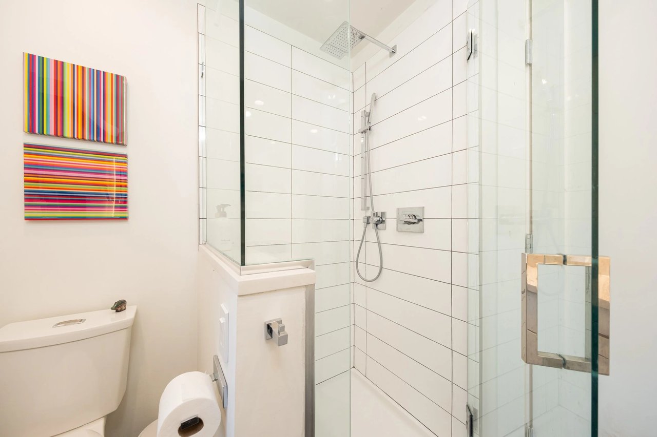 Renovated bathroom with a glass shower, white tile, chrome fixtures and colorful striped artwork.