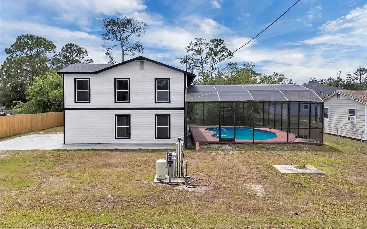 Rear of a two-story white house beside a screened swimming pool enclosure and broad backyard.