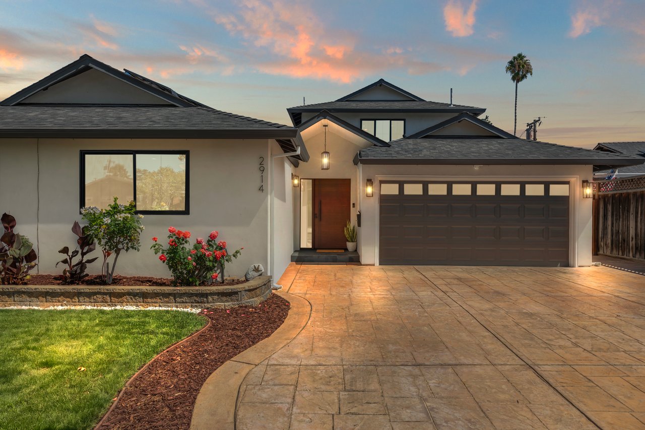 Home exterior at dusk with a stamped-concrete driveway, dark double garage, and landscaped front garden.