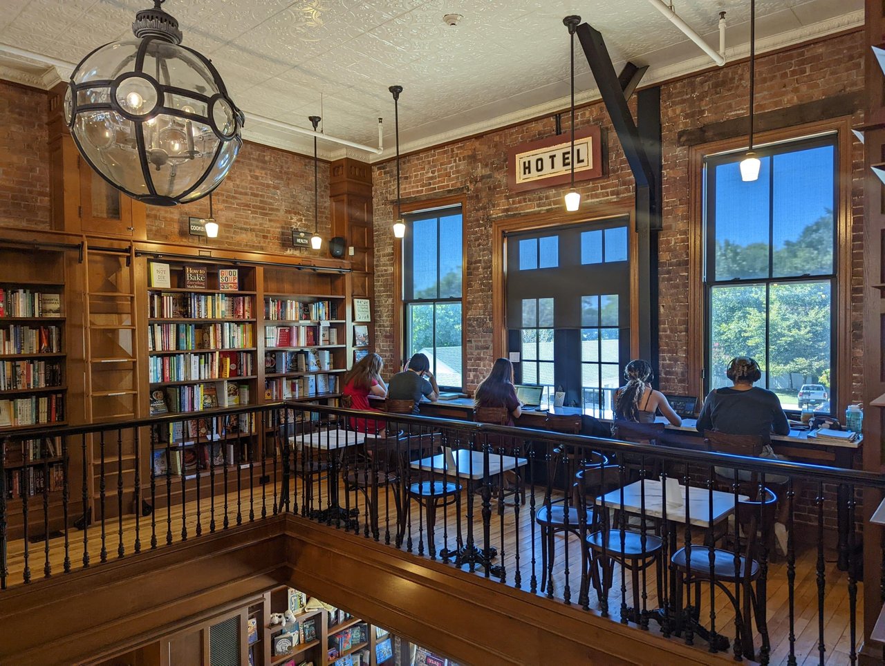 Bookstore with exposed brick, wooden bookshelves, and readers seated at a bright window counter.
