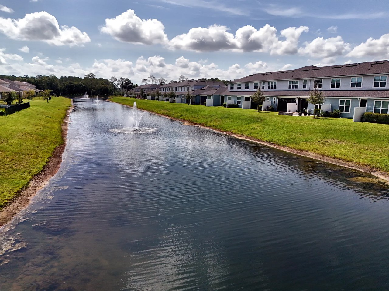 Attached homes line a pond with grassy banks and fountains.