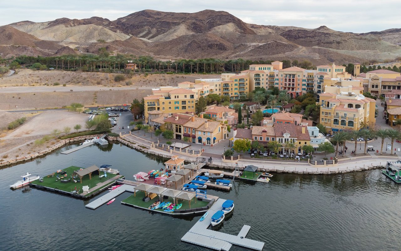 Waterfront resort community with a marina, Mediterranean-style buildings, and desert mountains.
