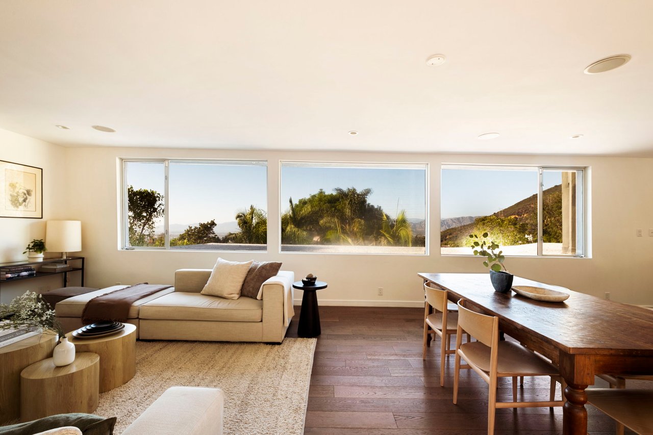 Living and dining room with wide windows overlooking greenery and hills.