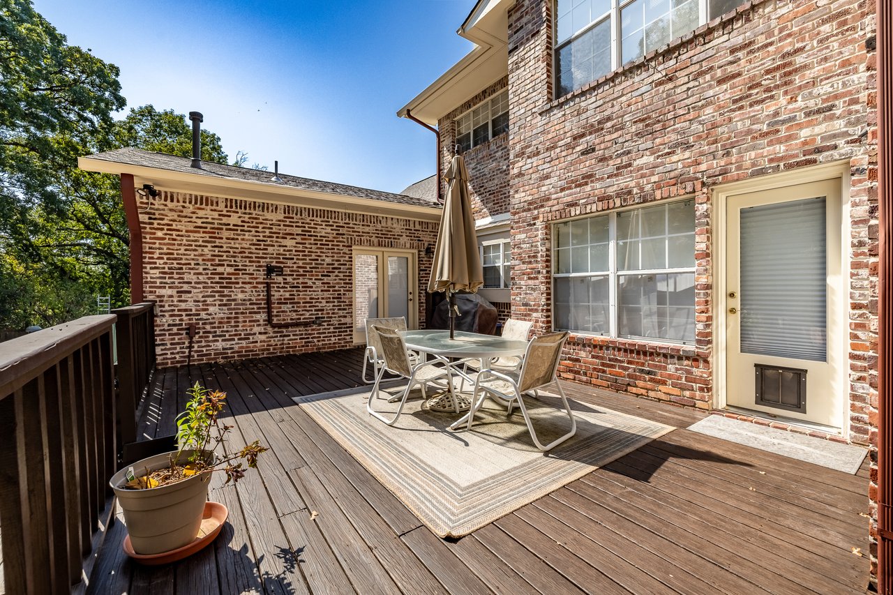 Wooden deck with patio dining set beside a brick house.