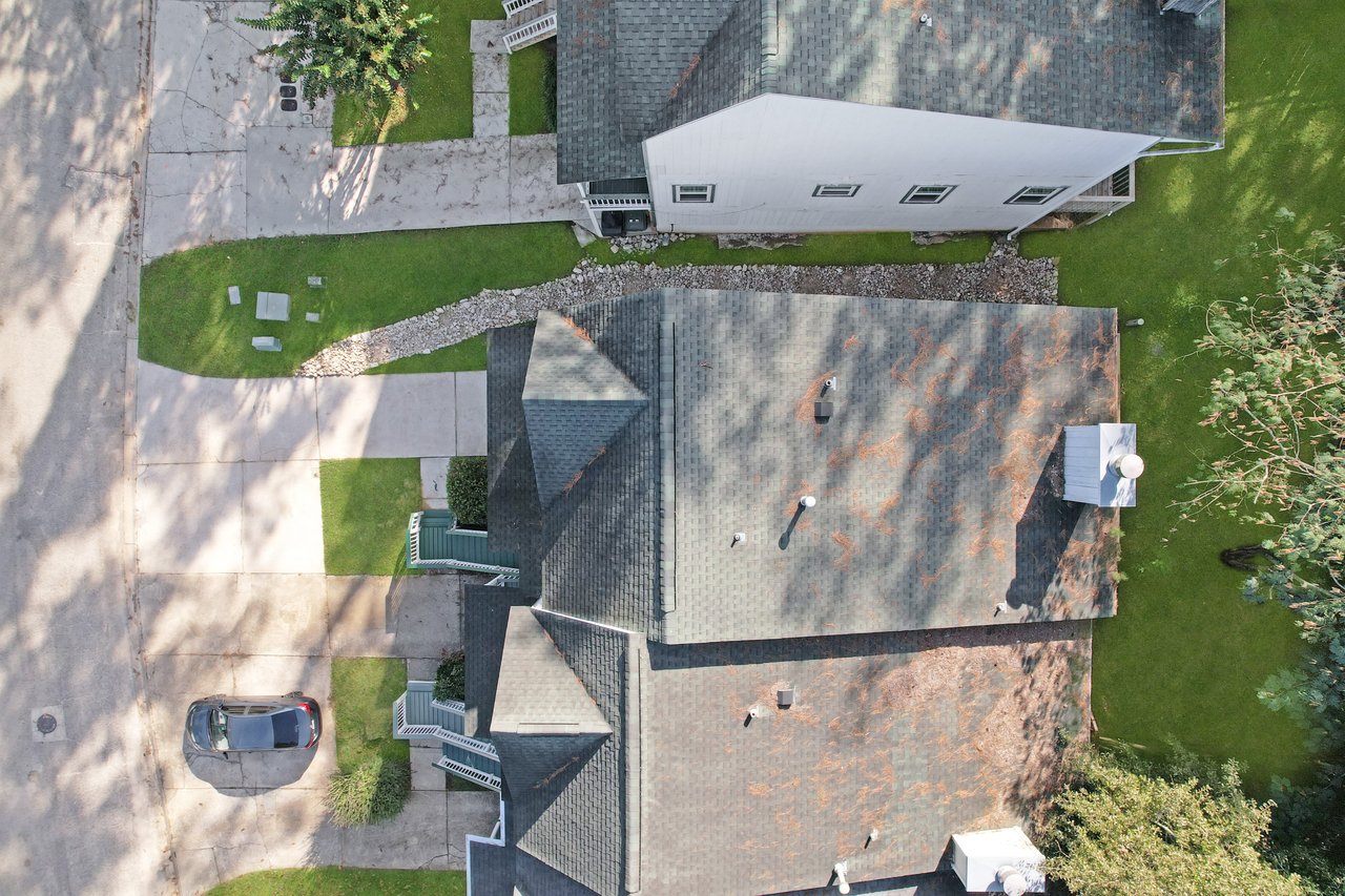 Aerial top-down view of the townhome at 529 Collinsford Road, Tallahassee, Florida, showing the roofline, driveway, and front walkway. The image captures the attached neighboring units, green lawn areas, and surrounding trees, providing a clear look at the property’s layout and roof condition.