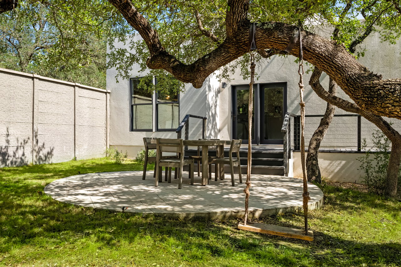 Backyard patio with an outdoor dining set beneath a large tree and a rope swing.