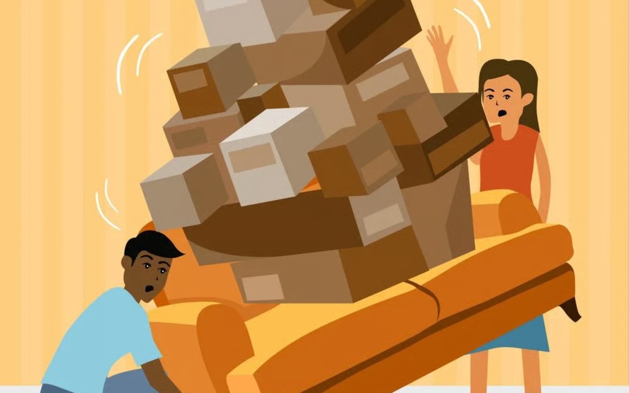 Two movers struggle to carry a couch overloaded with cardboard boxes.