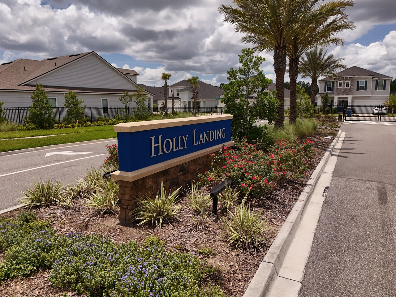 Holly Landing entrance sign beside landscaped flower beds and palm trees, with homes behind it.