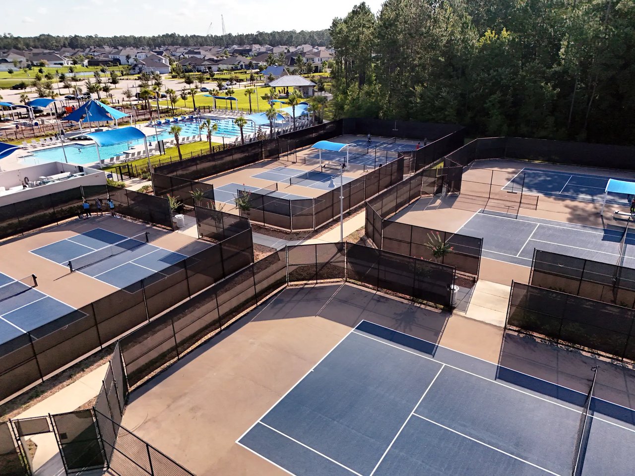 Fenced tennis and pickleball courts beside a community pool and playground.