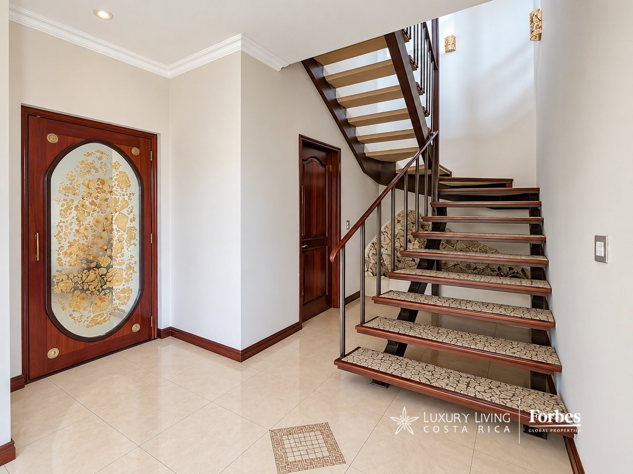 Entry hall with an ornate glass-paneled front door and a sweeping open-riser staircase.