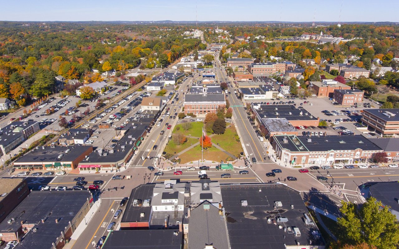 Aerial view of Needham town center, with a central green and autumn-colored trees.