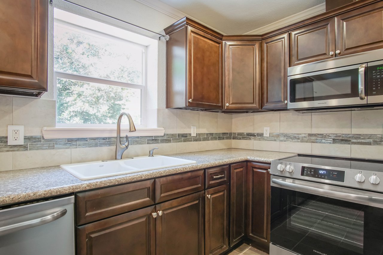 Modern kitchen with dark wood cabinets, stainless steel appliances, and a double sink under a large window. The ambiance is clean and inviting.