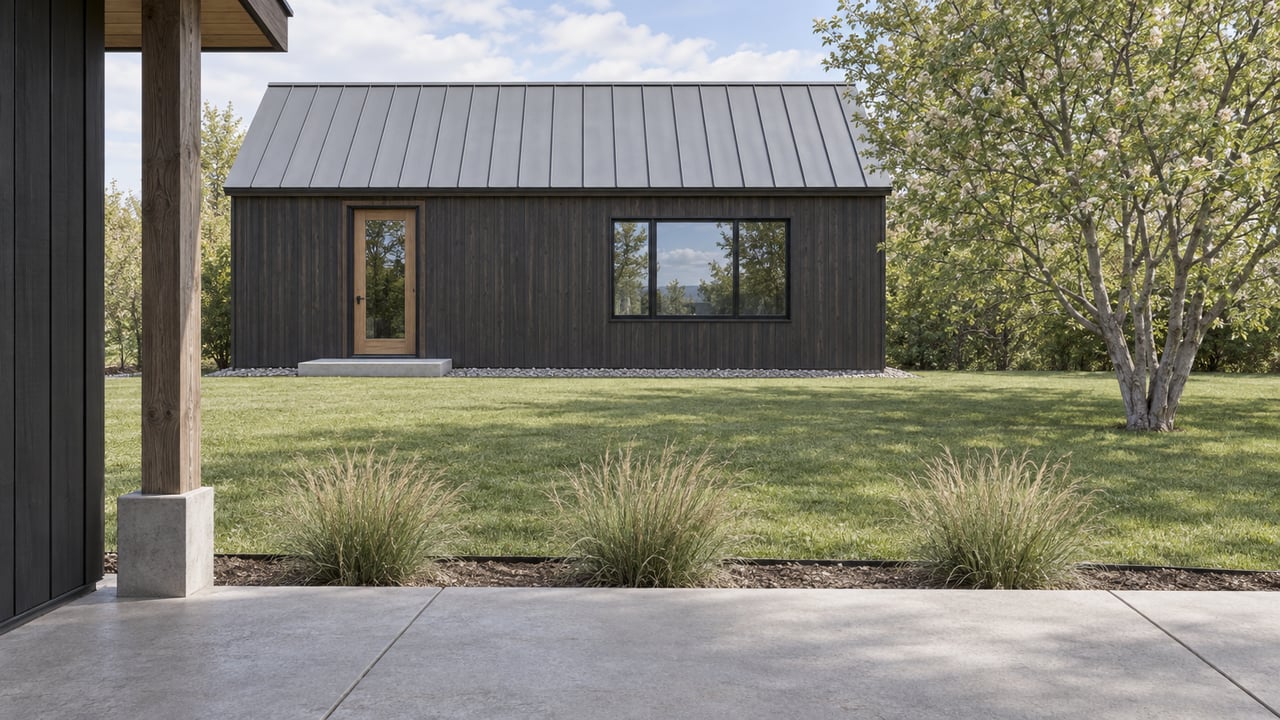 Compact cedar-clad backyard dwelling across a lawn, with a standing-seam roof and broad window.
