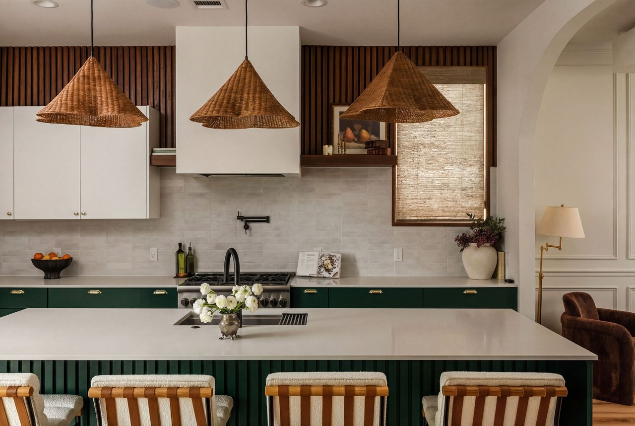 Modern kitchen with a white island, deep green cabinetry, and three woven pendant lights.