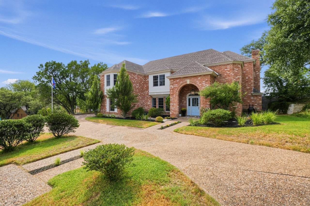 Two-story brick home with an arched entry, blue front door, and curving gravel driveway.