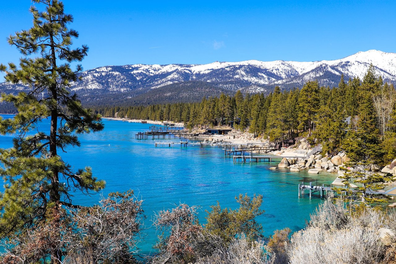 Incline Village shoreline with turquoise Lake Tahoe, docks, pine trees, and snow-covered mountains.