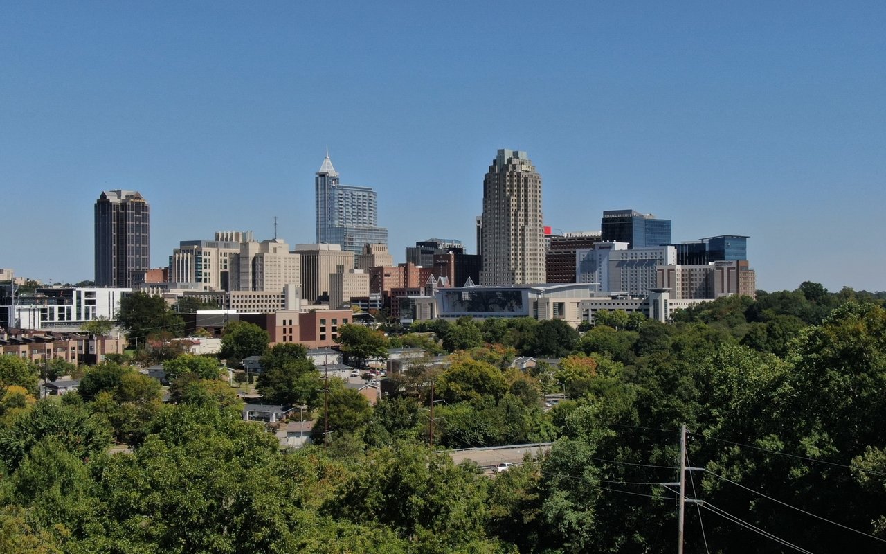 City skyline rising above leafy neighborhoods beneath a clear blue sky.