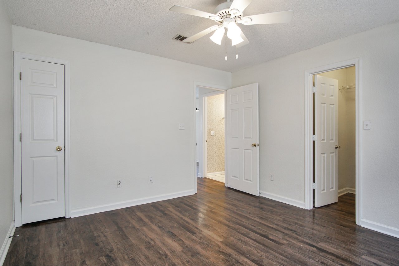 Empty room featuring hardwood floors and a ceiling fan, creating a spacious and airy atmosphere.