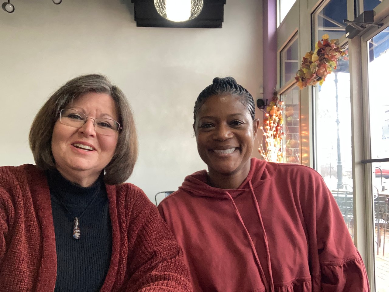 Two smiling women, Faith Rosenshein Young and Toni Browley seated side-by-side in the Scone House Cafe, Winfield, Illinois.