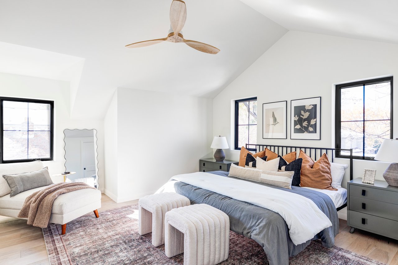 Master suite angle view with king-size bed, a plush white chaise lounge, and wooden panel ceiling fan