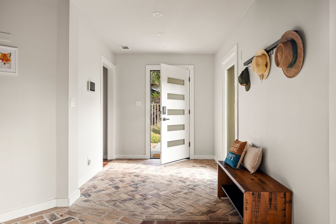 Entryway with an open front door, herringbone brick floor, and a wooden bench beneath wall-mounted hats.