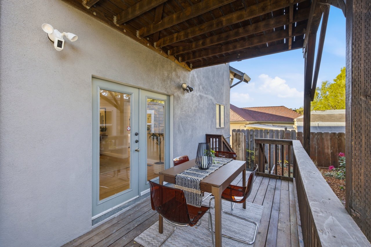 Covered wooden deck with a dining table and chairs beside glass doors.