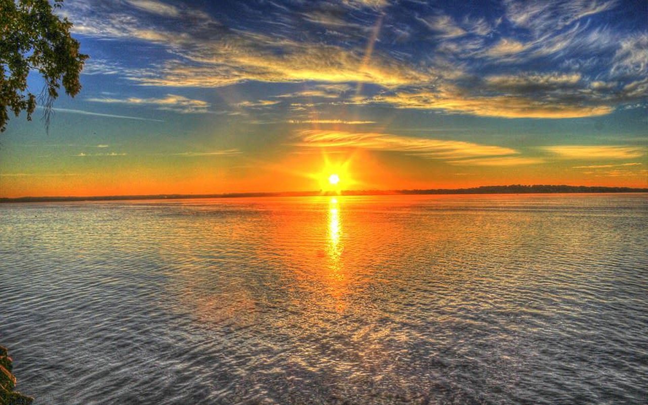 Sunset over a calm lake, with a golden reflection stretching across the water beneath dramatic clouds.