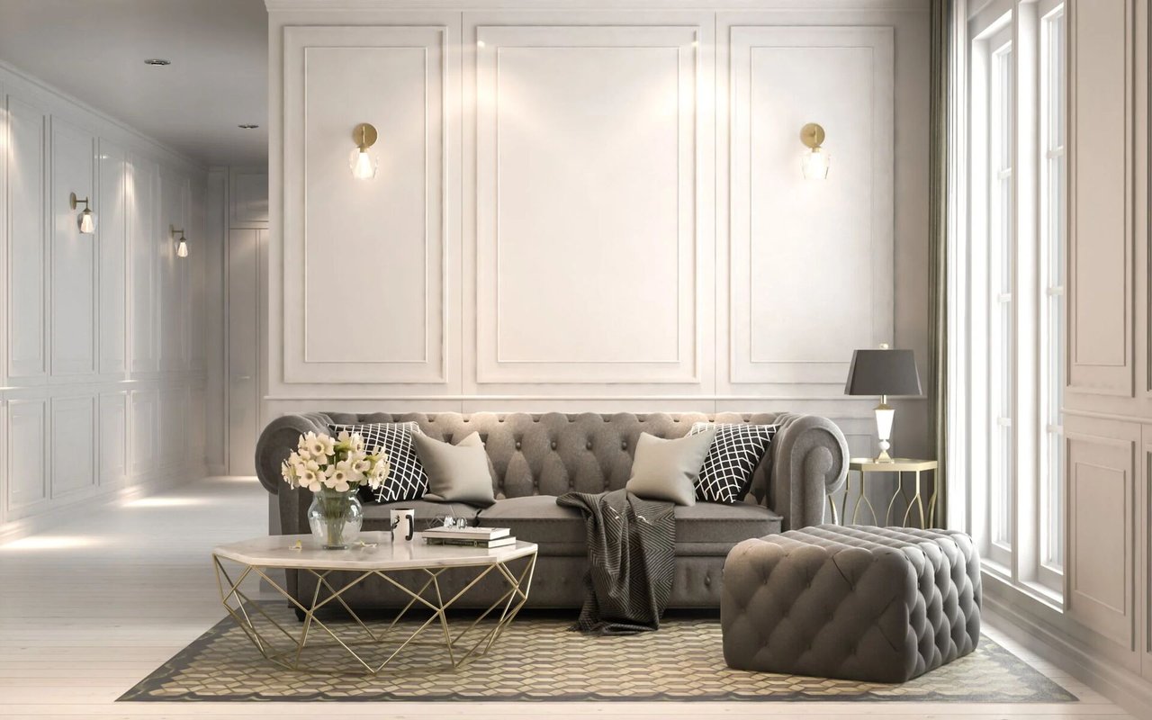 Bright living room with a tufted gray sofa, matching ottoman, and tall windows.