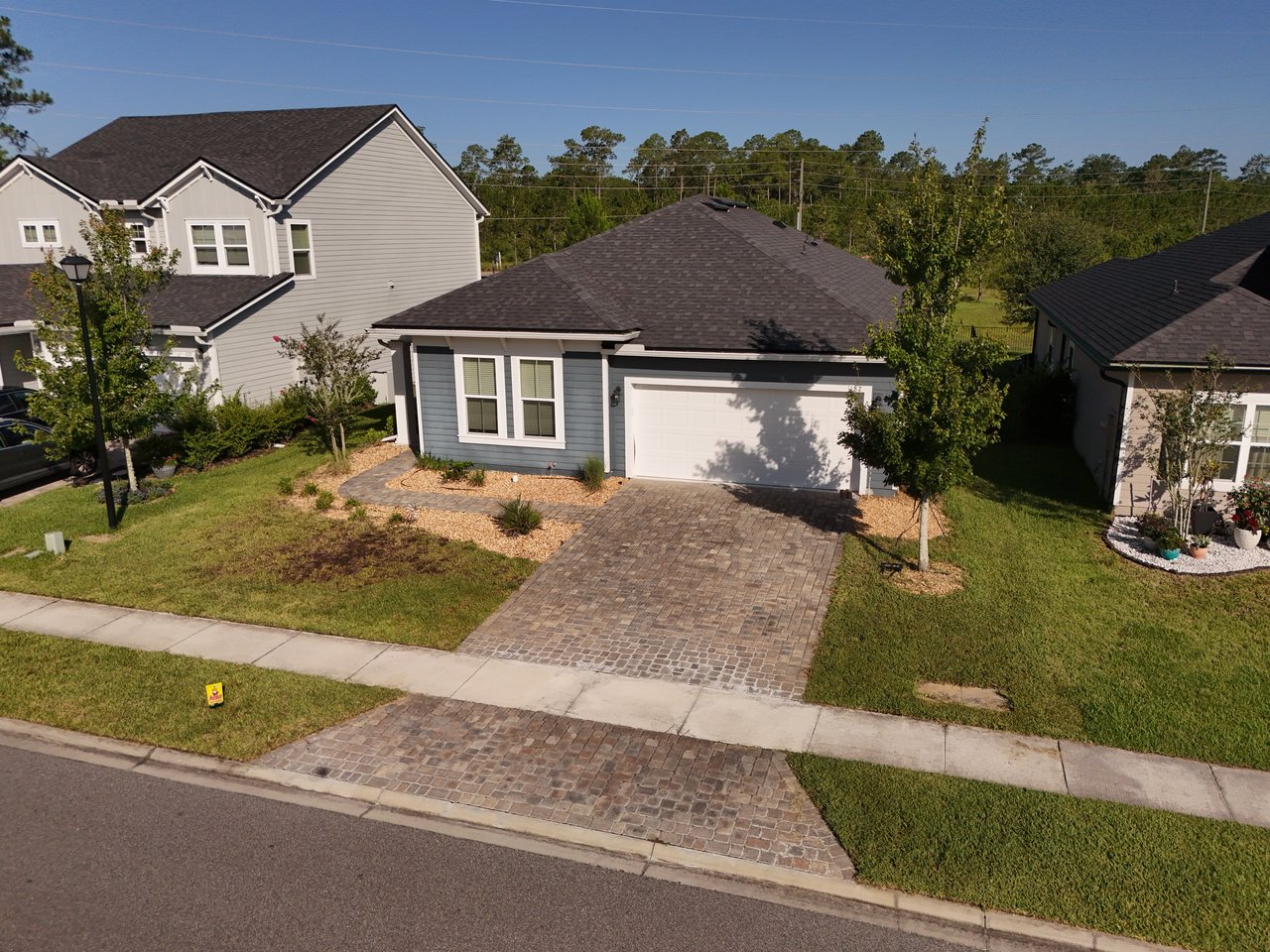 Blue-gray single-story home with a white double garage and paver driveway, viewed from above.