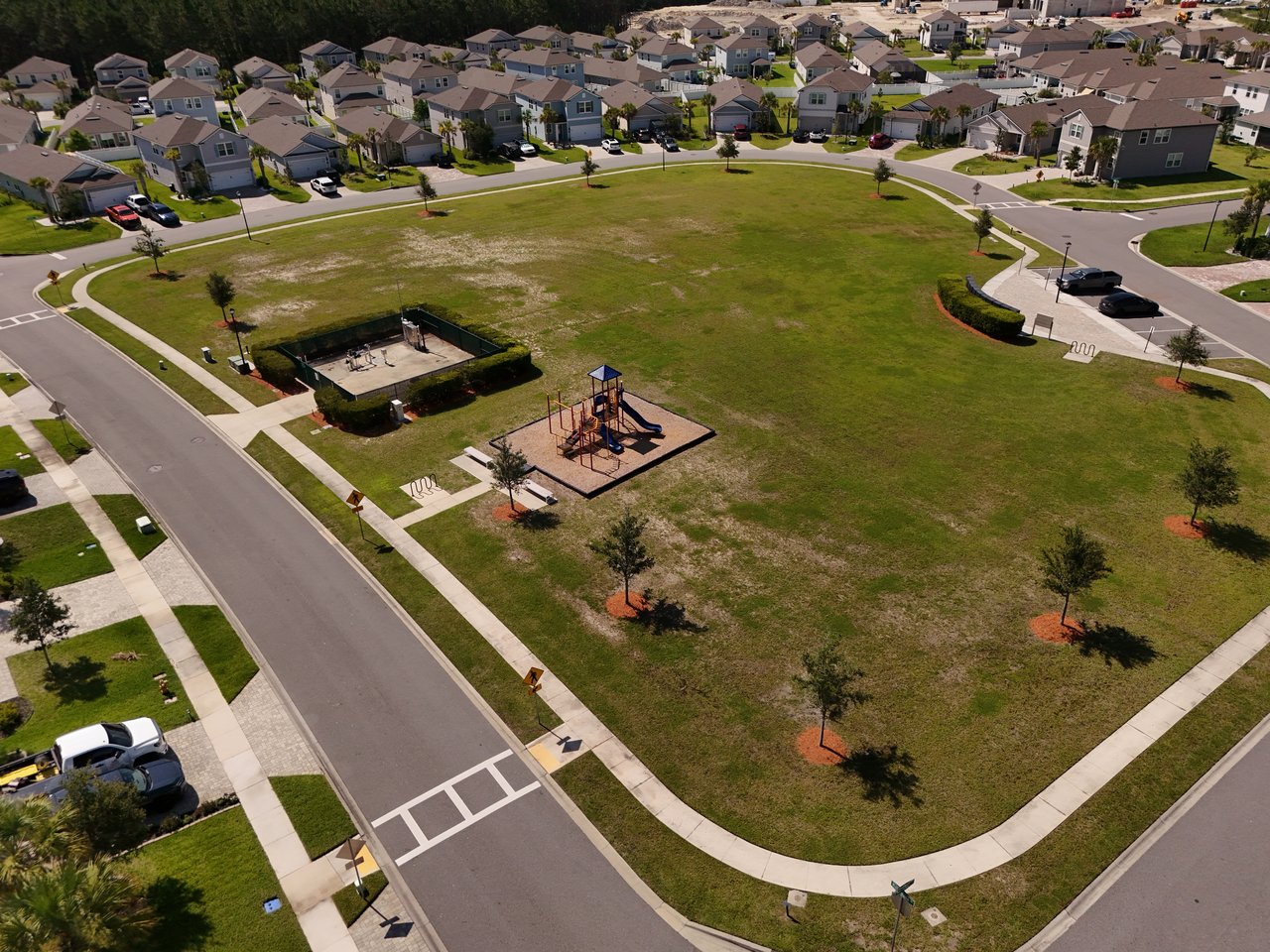 Aerial view of a neighborhood park with a playground, grassy open space, and surrounding homes.