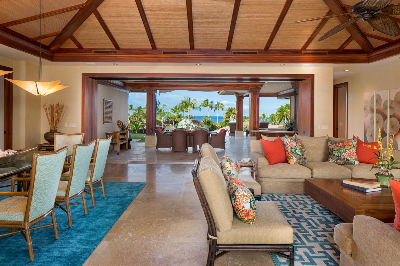 Open-plan living and dining room with a wood-beamed ceiling and ocean view beyond the palms.